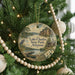 A round ornament hanging on a Christmas tree, featuring a scenic landscape with a lake, trees, and a cabin.