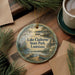 A decorative ornament with a lake and park scene, featuring a boat and a bird, is displayed on a wooden surface alongside a cup of coffee and some pine branches.