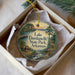 A decorative ornament in a box, featuring a scenic landscape with a lake, forest, and a deer.