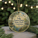 A round ornament with a painting of Lake Fausse Pointe State Park in Louisiana, featuring a bird and a pond, is displayed on a table with a blurred background of a Christmas tree.