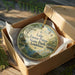 A round ornament in a box, featuring a scenic landscape with a lake, trees, and birds, along with the text "Lake Fausse Pointe State Park, Louisiana".