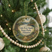 A round ornament hanging on a Christmas tree, featuring a scenic landscape with a lake, mountains, and a bird.
