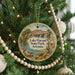 A round ornament hanging on a Christmas tree, featuring a scenic landscape with mountains, palm trees, and a bird.