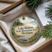 A round ornament with a scenic lake and forest landscape, featuring a canoe and a deer, is displayed in a box with pine branches.