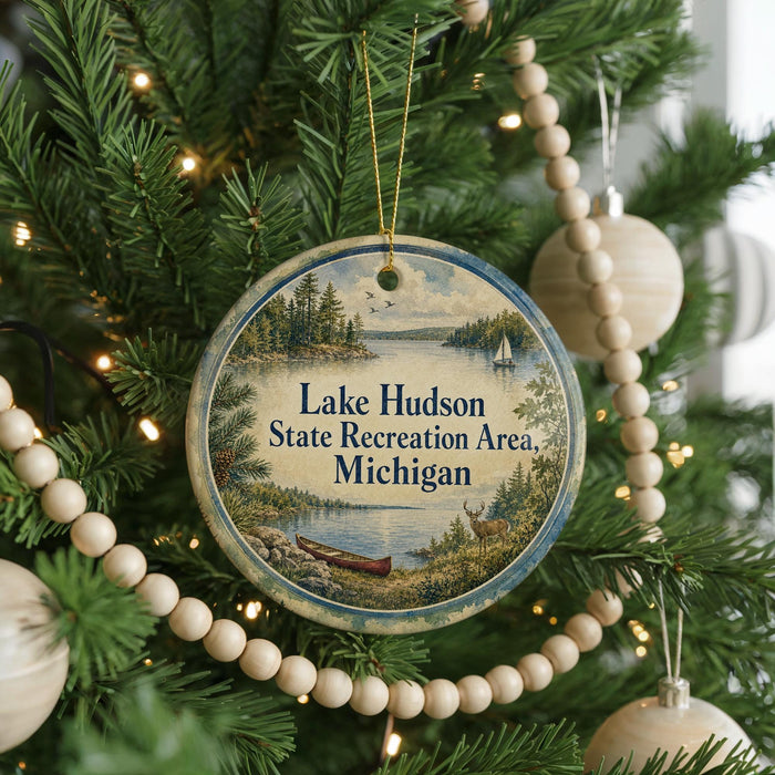 A round ornament hanging on a Christmas tree, featuring a scenic landscape with a lake, forest, and boats.