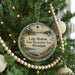 A round ornament hanging on a Christmas tree, featuring a scenic landscape with a lake, forest, and boats.