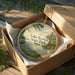 A decorative ornament in a box, featuring a scenic landscape with a lake, trees, and a boat, with the text "Lake Keomah State Park, Iowa" printed on it.