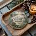 A decorative ornament with a scenic lake and state park image, featuring a bird, canoe, and pine cones, placed on a wooden tray alongside a lit candle.