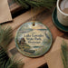 A decorative ornament with a lake and state park scene, featuring a canoe and a bird, is displayed on a wooden surface alongside a cup of coffee and some pine branches.