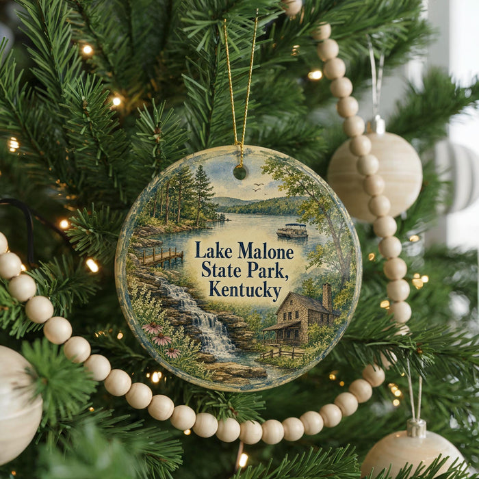 A round ornament hanging on a Christmas tree, featuring a scenic landscape with a waterfall and a house.