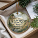 A decorative ornament with a lake and forest scene, featuring a loon and other wildlife, is displayed in a box with pine branches.