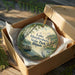 A round ornament in a box, featuring a scenic landscape with a lake, trees, and a bird, along with the text "Lake Murphysboro State Park, Illinois".