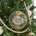 A circular ornament hanging on a Christmas tree, featuring a scenic landscape with a lake, a bridge, and a bird.