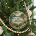 A round ornament hanging on a Christmas tree, featuring a scenic image of a lake, a bridge, and a bird.