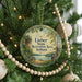A round ornament hanging on a Christmas tree, featuring a scenic landscape with a lake and a picnic table.