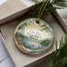 A decorative ornament with a scenic landscape of a lake, pine trees, and mountains, featuring the text "Lily Bay State Park, Maine".