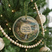 A round ornament hanging on a Christmas tree, featuring a scenic landscape with a waterfall and mountains.