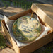 A decorative ornament in a box, featuring a scenic landscape with a waterfall and a tower, with the text "Lincoln Trail State Park, Illinois" printed on it.