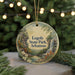 A circular ornament with a scenic landscape of Loggy State Park, Arkansas, featuring a waterfall and pine trees, is displayed on a table with Christmas lights in the background.