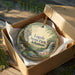 A decorative ornament in a brown box, featuring a scenic landscape with a waterfall and trees, with the text "Logoy State Park, Arkansas" printed on it.