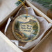 A decorative ornament in a box, featuring a scenic landscape with mountains, trees, and a lake.