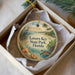 A circular ornament with a beach scene and a bird is displayed in a box.