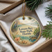 A round ornament with a beach scene and a bird is displayed in a box, surrounded by pine branches.