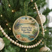 A round ornament hanging on a Christmas tree, featuring a tropical beach scene with palm trees, a bird, and a sunset.