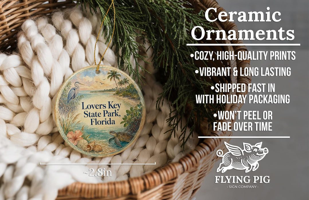 Ceramic ornaments, including a round ornament with a tropical scene and text, are displayed in a basket with greenery.