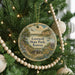 A round ornament hanging on a Christmas tree, featuring a scenic landscape with a house, trees, and a body of water.
