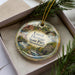 A decorative ornament with a scenic image of Lowell Heritage State Park in Massachusetts, featuring a river, buildings, and greenery.