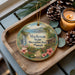 A wooden tray with a decorative ornament featuring a tropical landscape, including a waterfall, palm trees, and flowers, along with pine cones and a lit candle.