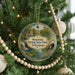A round ornament hanging on a Christmas tree, featuring a scenic image of Mammoth Spring State Park in Arkansas.