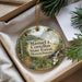 A round ornament with a scenic forest landscape, featuring pine trees, a waterfall, and a path, is displayed in a box with pine branches.