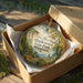 A decorative ornament in a wooden box, featuring a scenic landscape with a mountain, trees, and a lake.