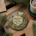 A decorative ornament featuring a scenic image of the Maquoketa Caves State Park, Iowa, with a cup of coffee and pine branches in the background.
