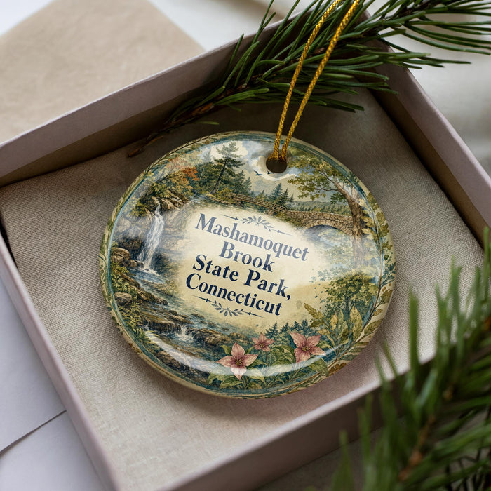 A decorative ornament in a box, featuring a scenic landscape with a waterfall and pine trees.