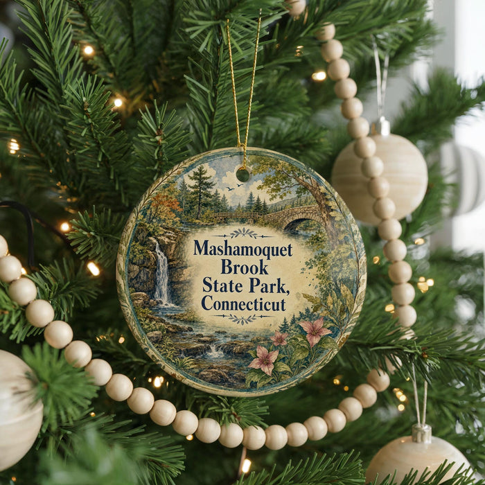 A round ornament hanging on a Christmas tree, featuring a scenic landscape with a waterfall and a bridge.