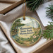 A decorative ornament with a scenic landscape of a lake, trees, and a castle, hanging from a string.
