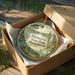 A circular ornament with a scenic landscape of Massasoit State Park, Massachusetts, displayed in a wooden box with a gold string.