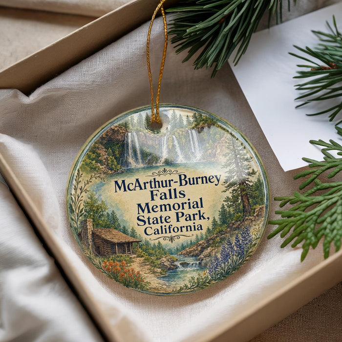 A decorative ornament with a scenic landscape featuring a waterfall, forest, and a cabin, hanging from a string.