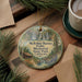 A round ornament with a scenic illustration of a waterfall and forest, hanging on a wooden surface.