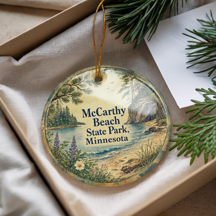 A decorative ornament with a scenic landscape of McCarty Beach State Park, Minnesota, featuring pine trees, a lake, and a sandy beach.