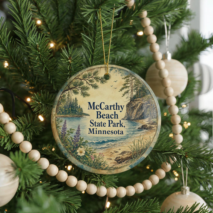 A round ornament hanging on a Christmas tree, featuring a scenic landscape with pine trees, a lake, and mountains.