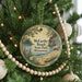 A round ornament hanging on a Christmas tree, featuring a scenic landscape with pine trees, a lake, and mountains.