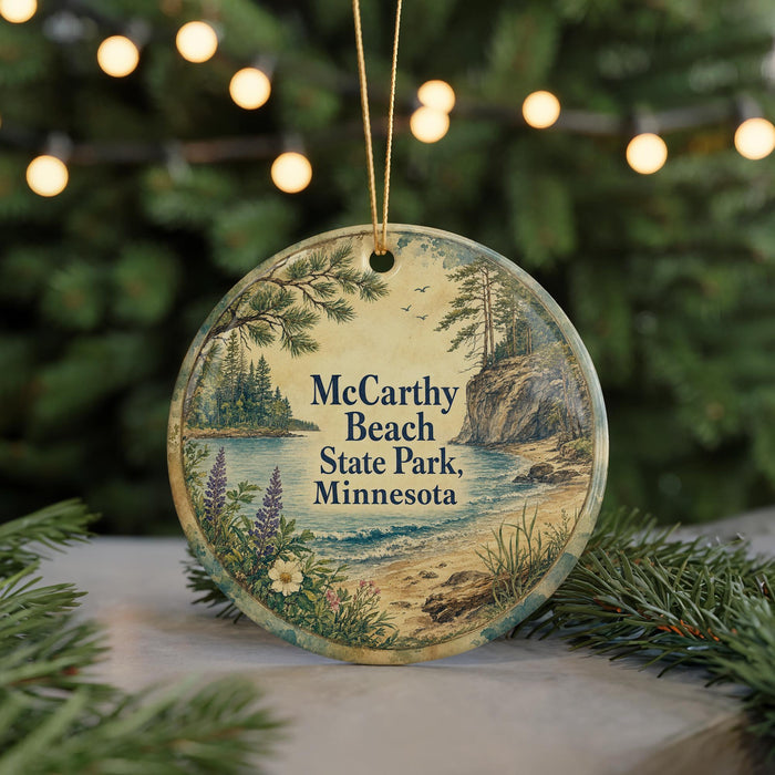 A round ornament with a scenic landscape of McCarty Beach, Minnesota, featuring pine trees, a lake, and a mountain.