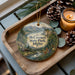 A decorative ornament featuring a scenic landscape of McCrokey State Park, Idaho, with pine cones and a lit candle on a wooden tray.
