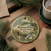 A decorative ornament featuring a scenic landscape with a waterfall, surrounded by pine branches and a cup of coffee on a wooden surface.