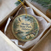 A circular ornament with a scenic image of a park, featuring a bird, a bridge, and flowers, is displayed in a box.
