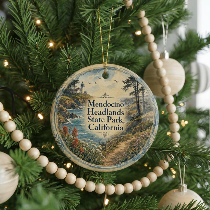 A round ornament hanging on a Christmas tree, featuring a scenic landscape with a lighthouse and a path leading through the greenery.